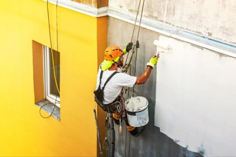 Rope-access painter applying exterior paint to a building facade